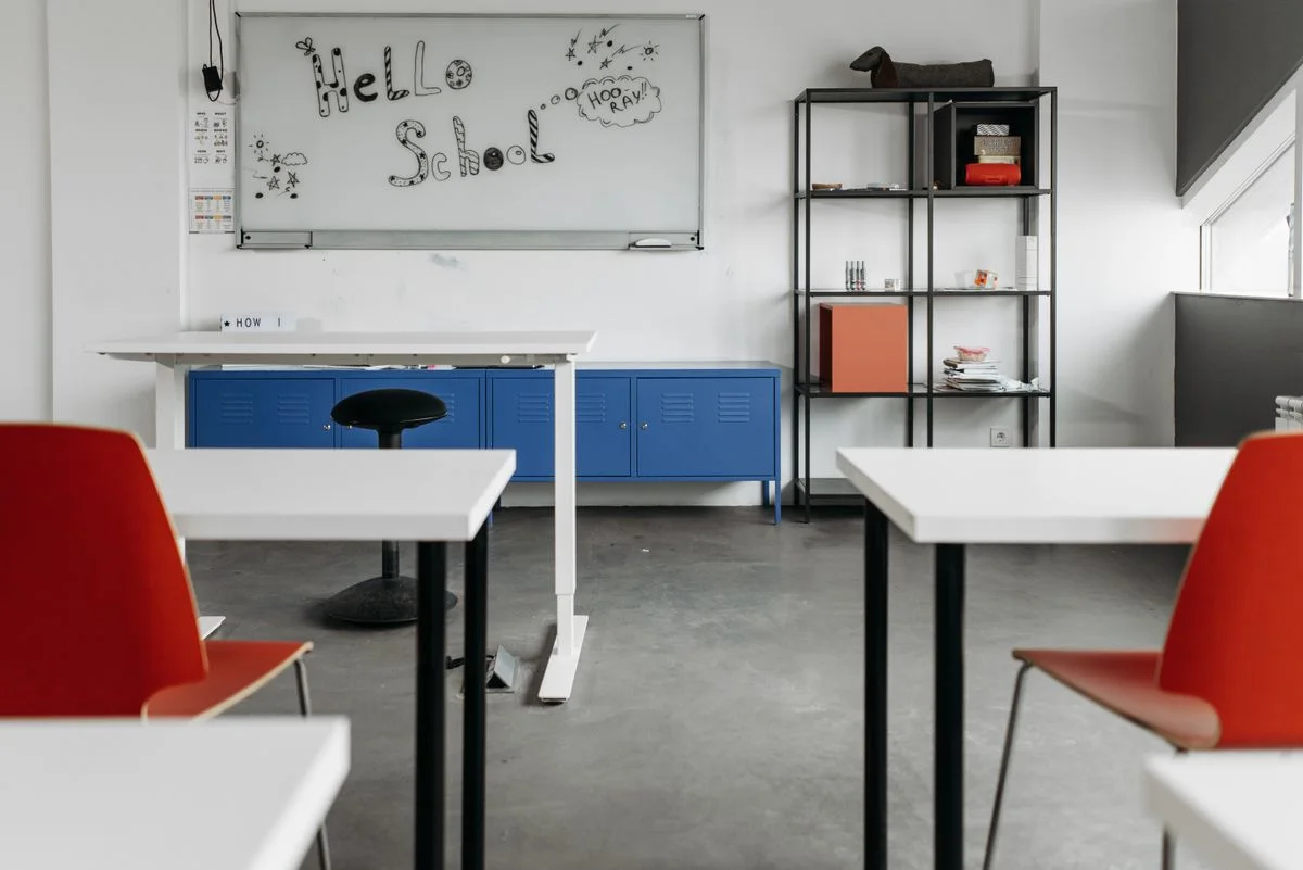 A bright contemporary classroom with white desks, red chairs and open shelving