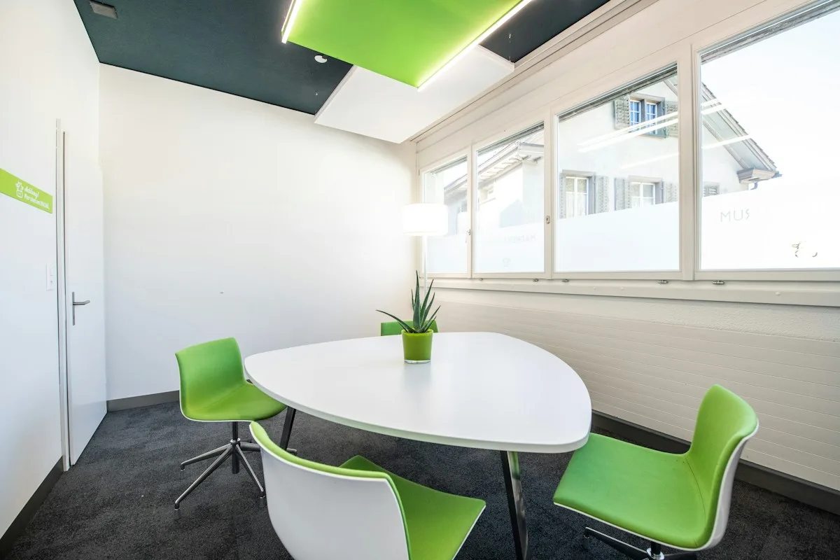 A light shared meeting room with a table and green chairs